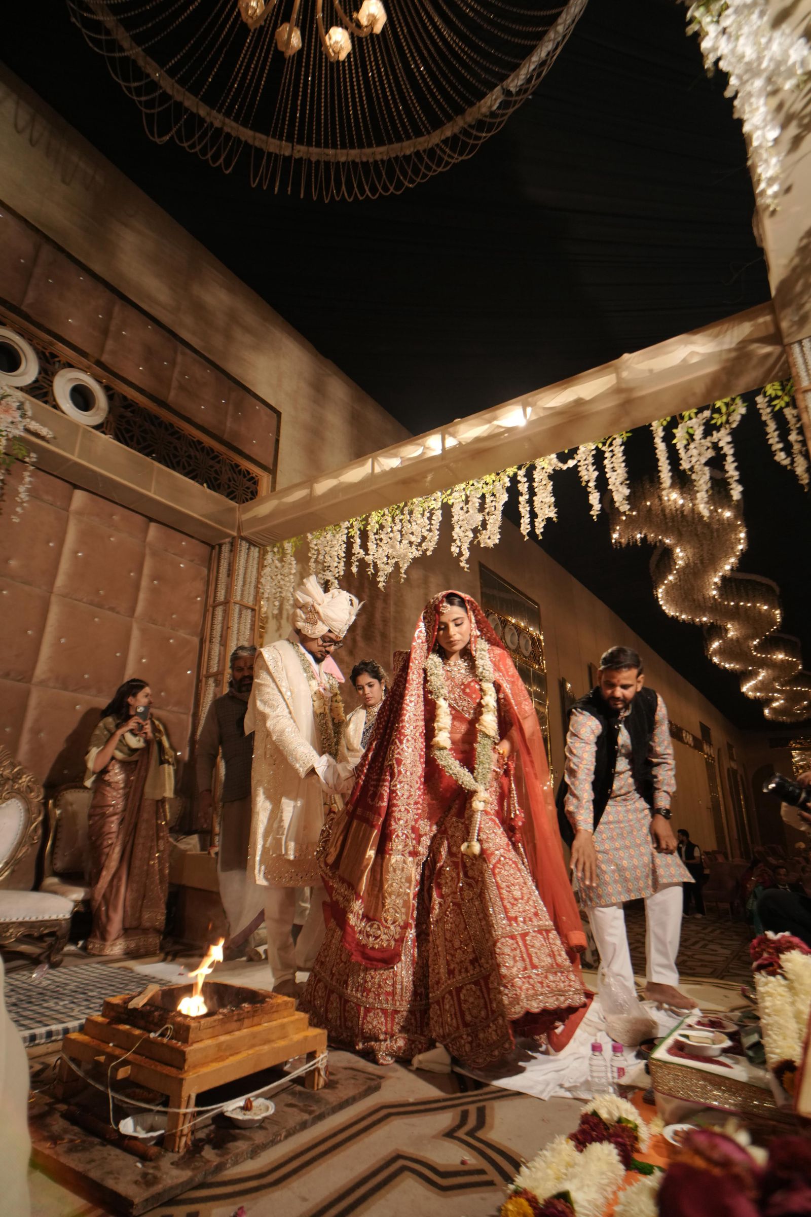 A bride in embroidered red beneath a chandelier at a ceremony