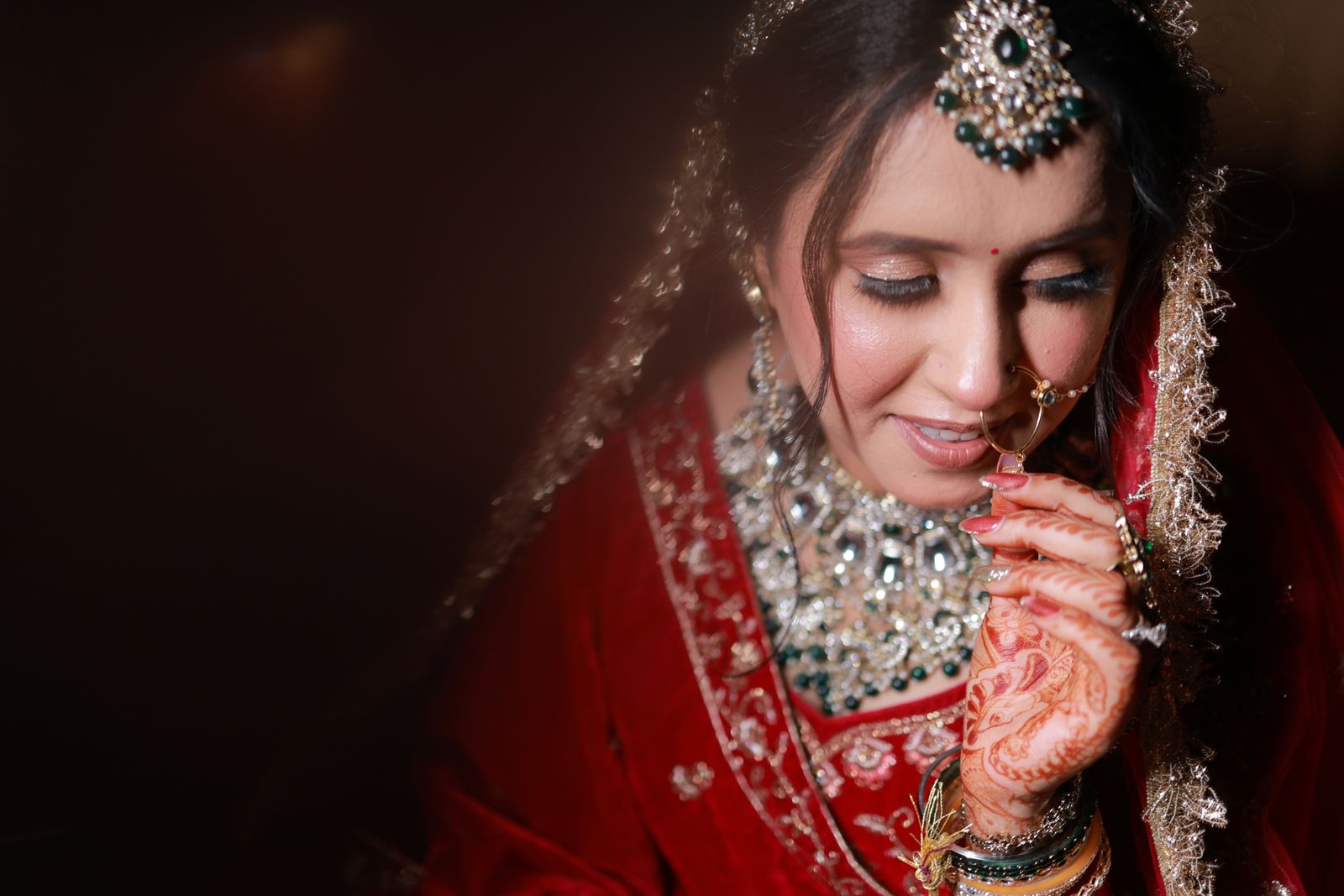 A bride in deep red, smiling softly with henna-adorned hands