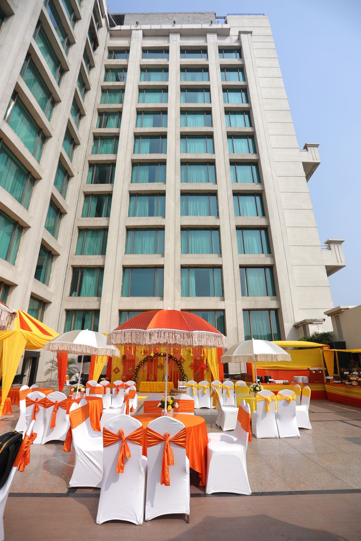 An outdoor wedding setup in ivory and marigold beneath a hotel façade